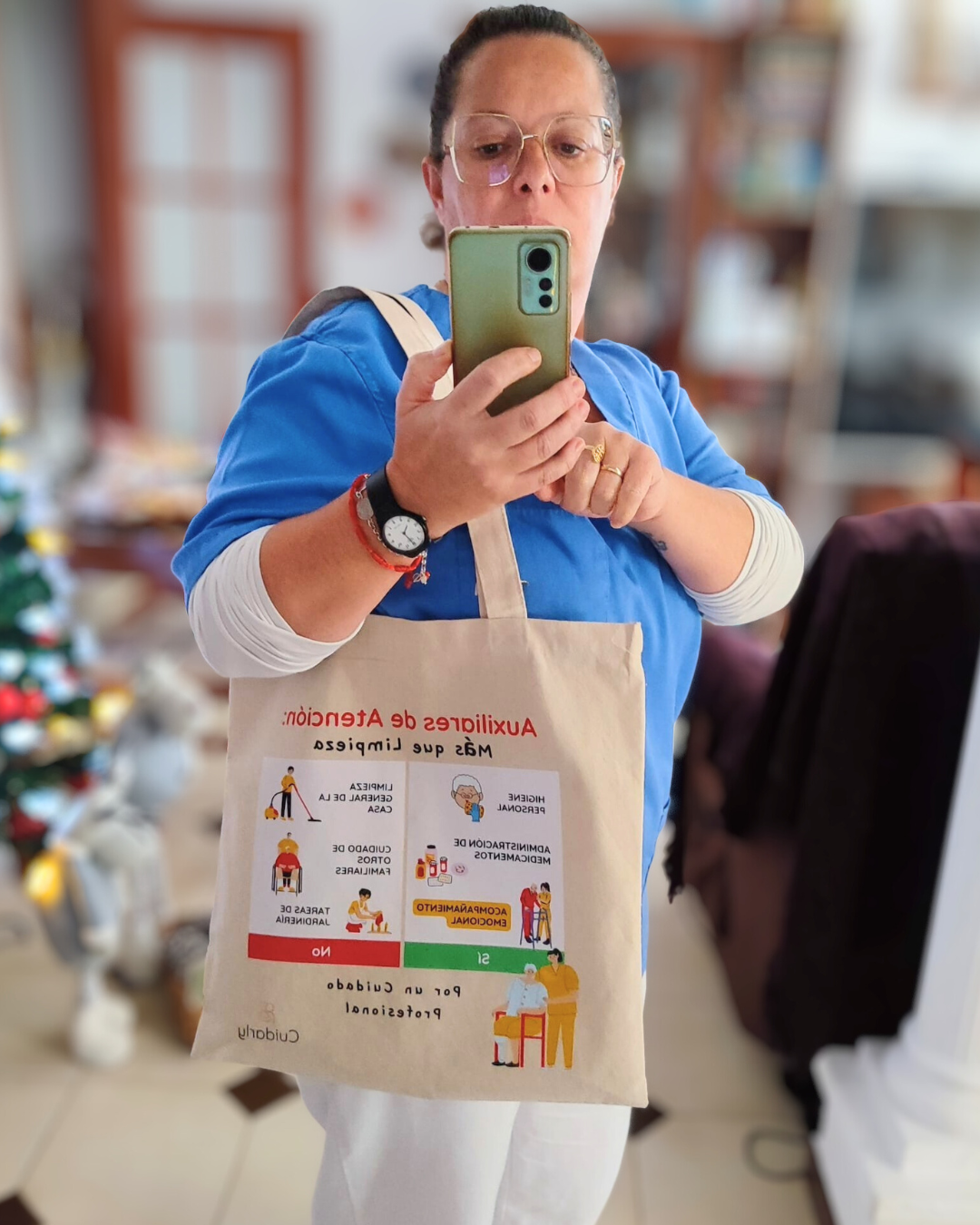 Auxiliar con camiseta azul y gafas posando con la totebag de Cuidarly frente al espejo.