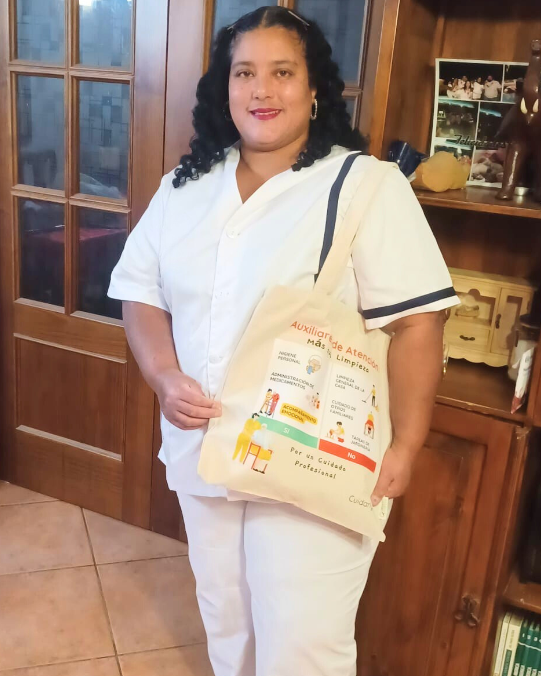 Auxiliar de ayuda a domicilio de pie en casa, sonriendo con su totebag Cuidarly.