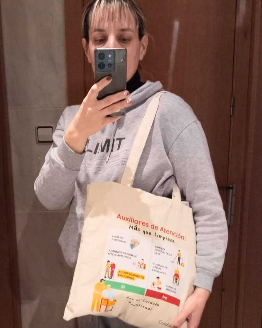 Auxiliar de ayuda a domicilio mostrando con orgullo su totebag Cuidarly frente al espejo.