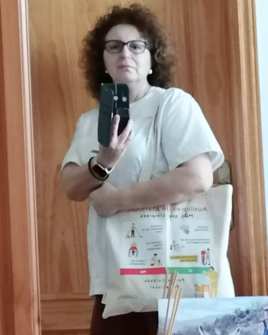 Mujer auxiliar de ayuda a domicilio se fotografía frente a un espejo con su totebag Cuidarly colgada al hombro, mostrando con firmeza su identidad profesional.