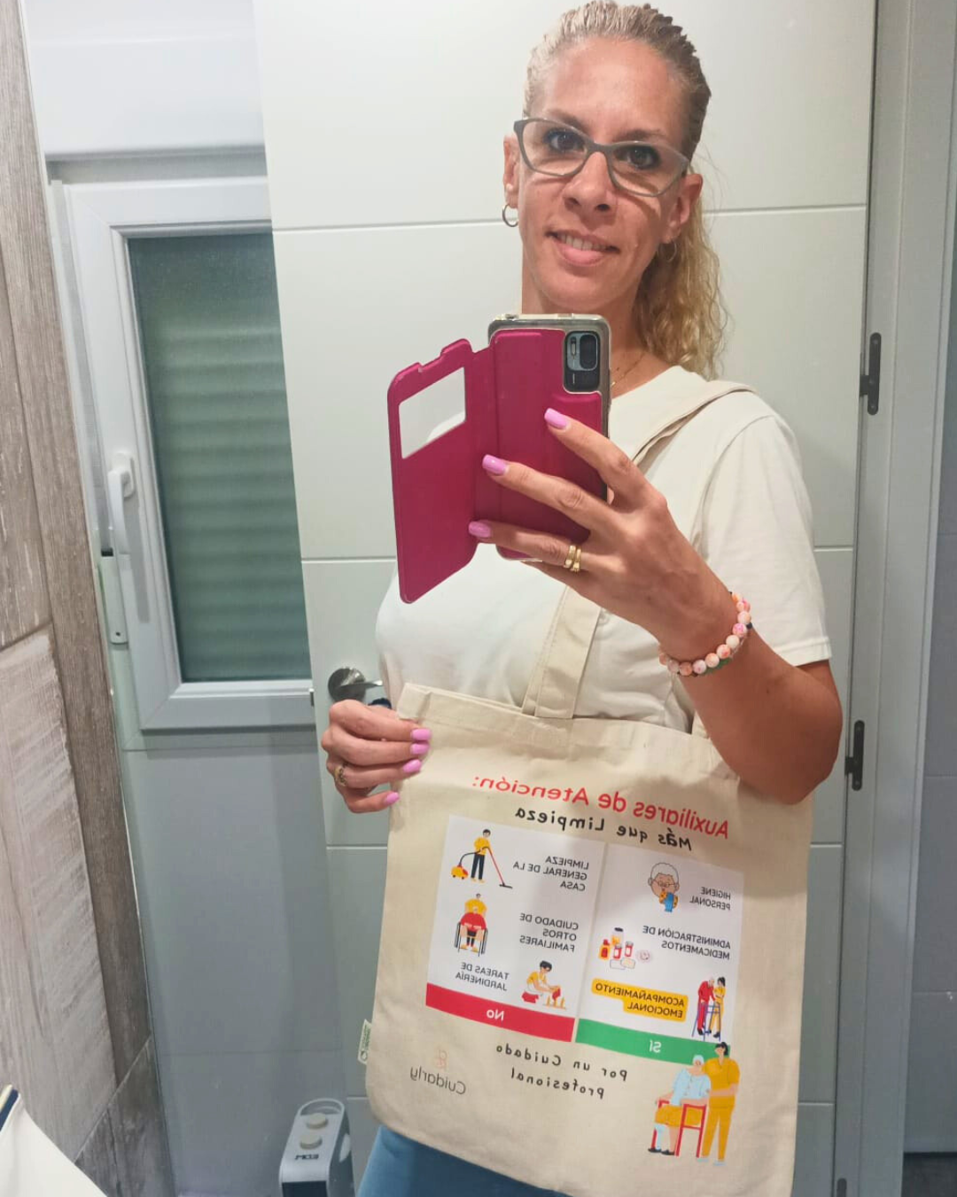 Mujer auxiliar de ayuda a domicilio se toma una foto frente al espejo mostrando su totebag de Cuidarly, símbolo de profesionalismo y compromiso.