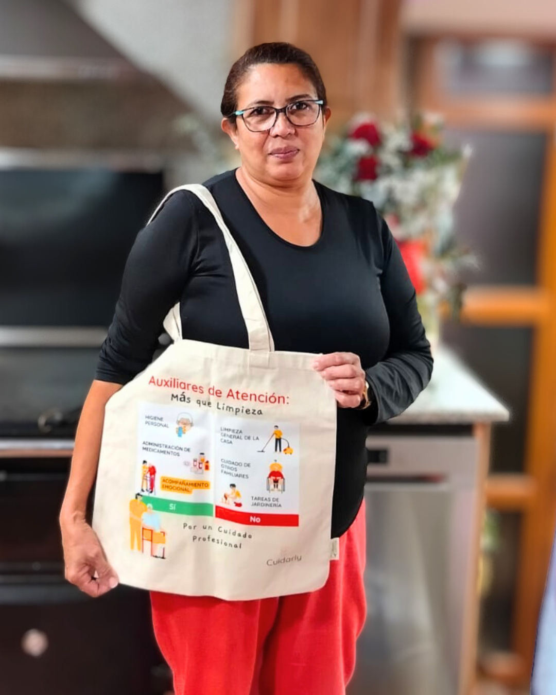 Mujer con gafas, camiseta negra y totebag de Cuidarly posando en la cocina con actitud decidida.