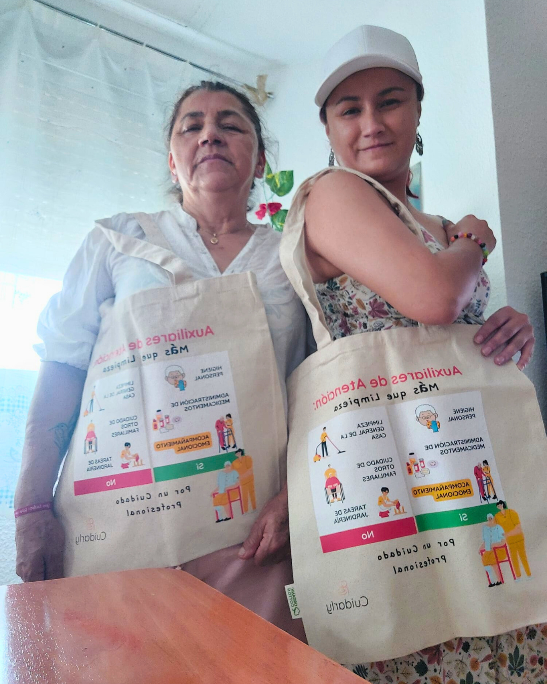 Dos auxiliares de ayuda a domicilio mostrando su totebag con mensajes reivindicativos.
